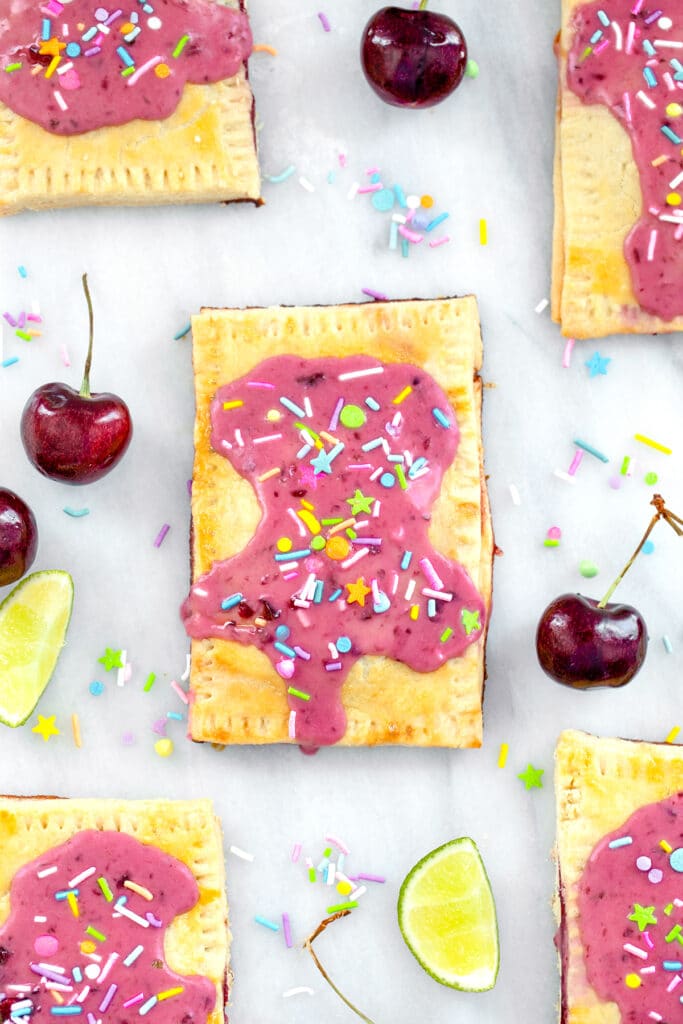Overhead view of a cherry lime pop tart on a marble surface with more pop tarts, cherries, limes, and sprinkles all around