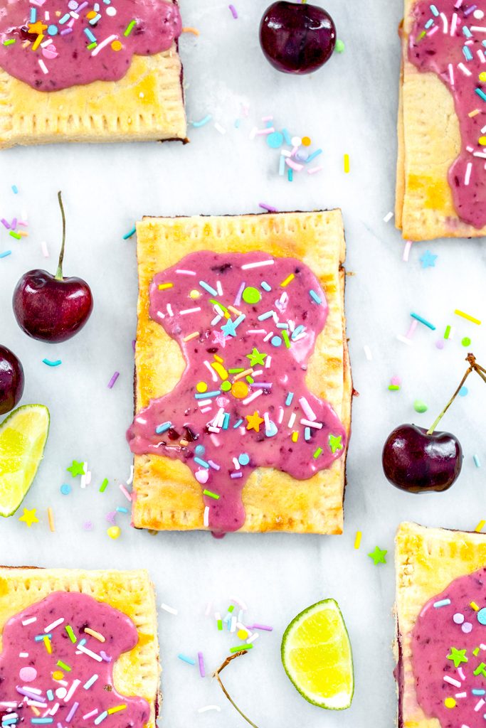 Overhead view of a cherry lime pop tart on a marble surface with more pop tarts, cherries, limes, and sprinkles all around