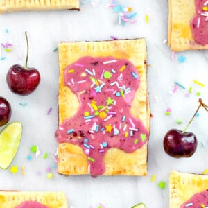 Overhead close-up view of a cherry lime pop tart on a marble surface with more pop tarts, cherries, limes, and sprinkles all around