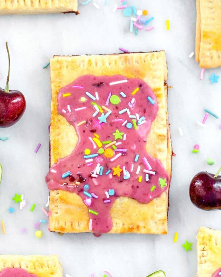 Overhead close-up view of a cherry lime pop tart on a marble surface with more pop tarts, cherries, limes, and sprinkles all around