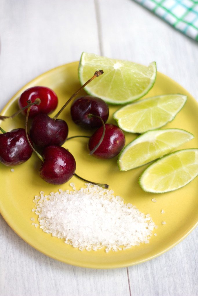 Overhead closeup view of yellow plate with sea salt, fresh cherries, and lime wedges
