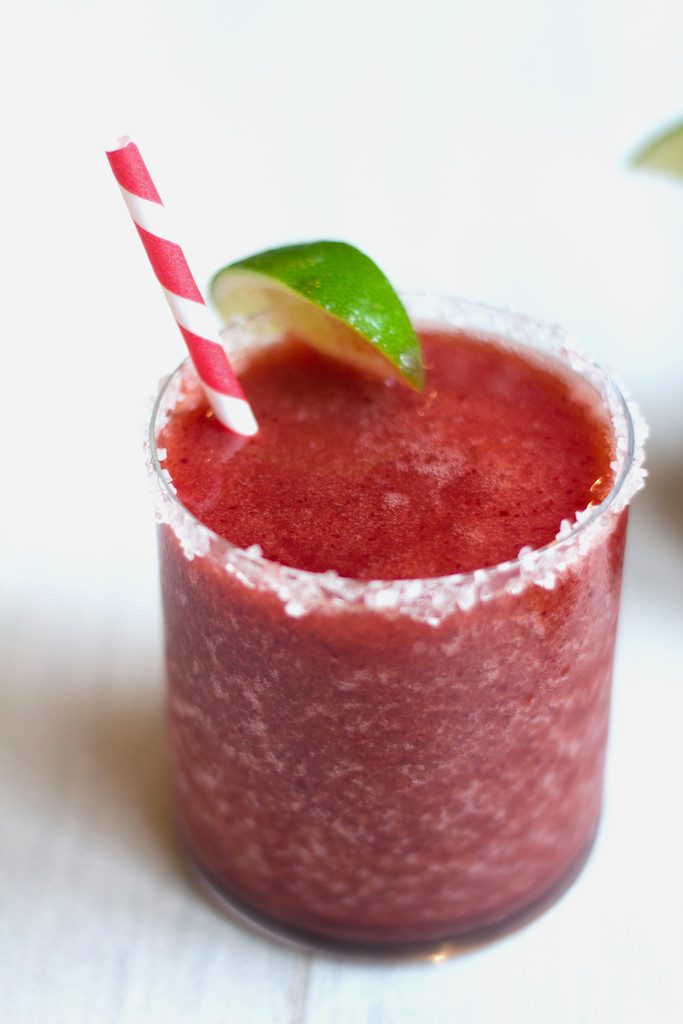 Head-on closeup view of a cherry margarita with lime wedge garish, salted rim and red and white straw