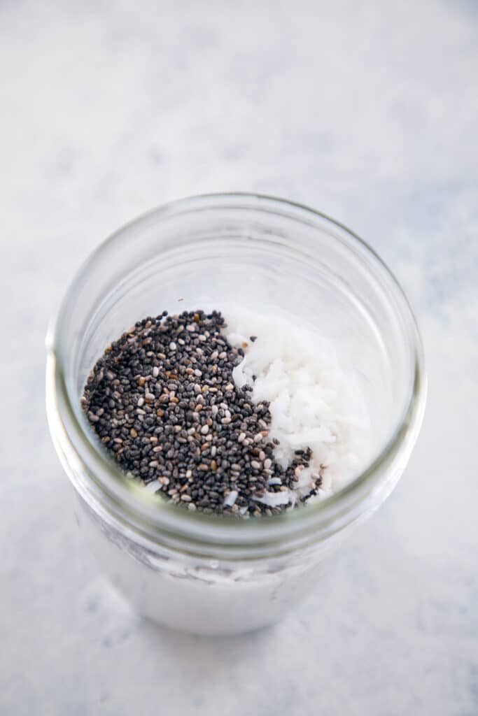 Coconut milk, chia seeds, and shredded coconut in a jar before mixing for chia pudding