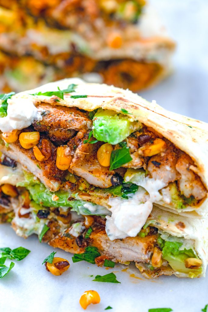 Close-up head-on view of a chicken, avocado, and corn burrito with feta sauce cut in half to show all of the ingredients