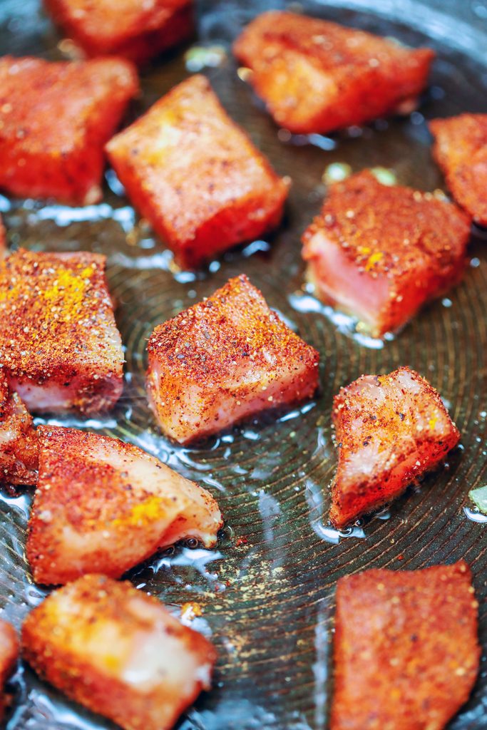 Cubed chicken breasts covered in spice cooking in oil in a skillet