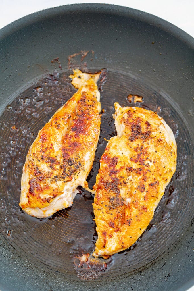 Overhead view of two seasoned chicken breasts in skillet