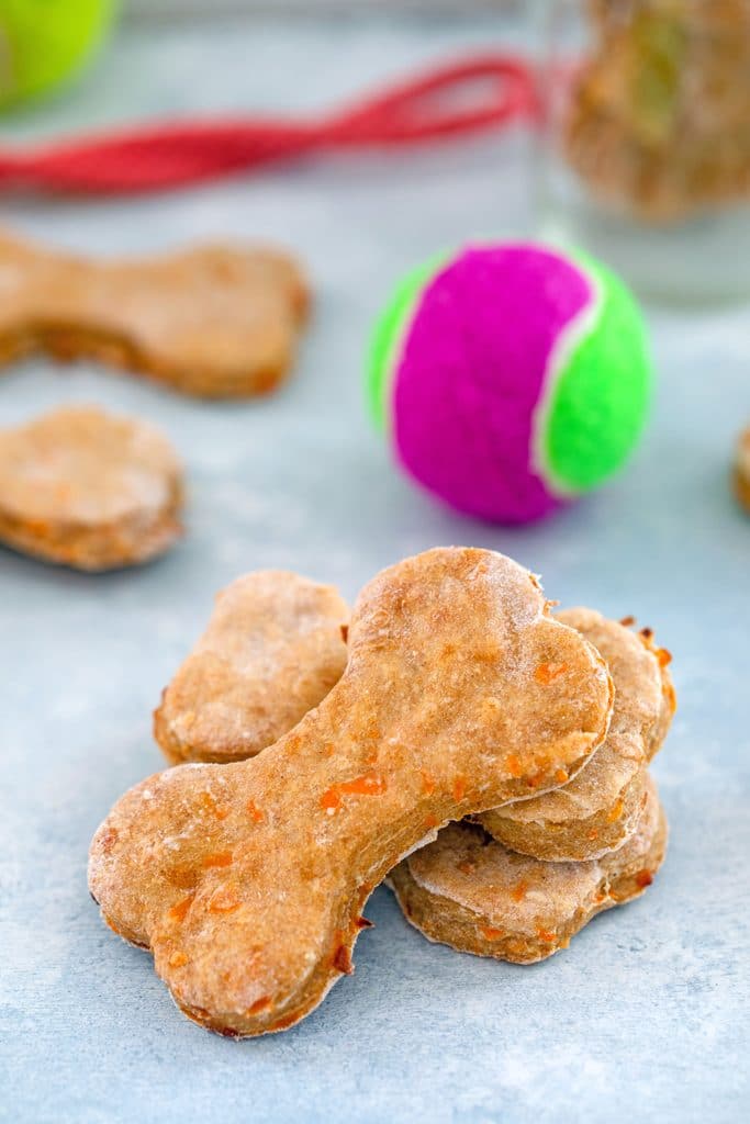 Head-on view of chicken dog treats stacked together with more in the background, along with a tennis ball and leash