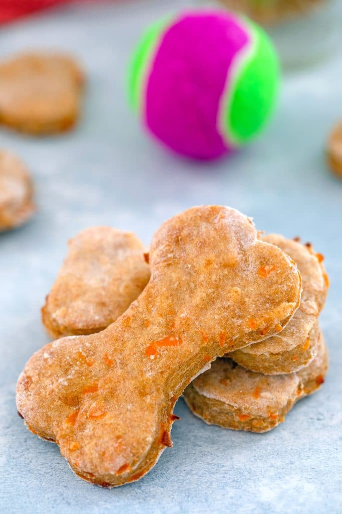 Close-up head-on view of chicken dog treats with more treats and a tennis ball in the background