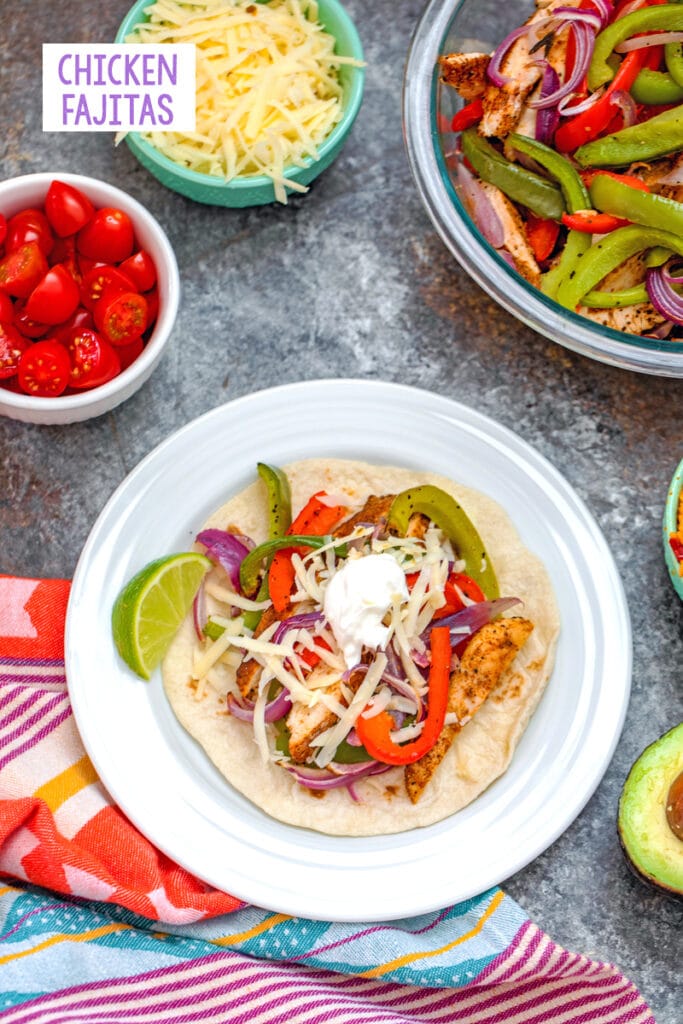 Overhead view of a prepared chicken fajita on a plate surrounded by a bowl of sliced chicken and vegetables and bowls of toppings with recipe title at top