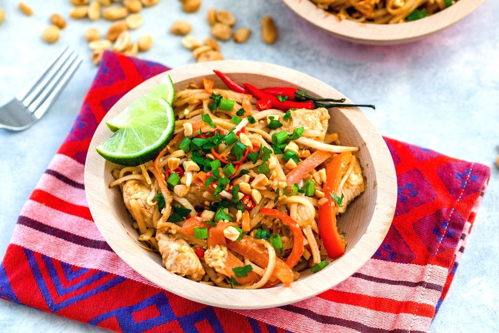 Landscape closeup view of bowl of chicken Pad on a red towel with fork and peanuts in the background