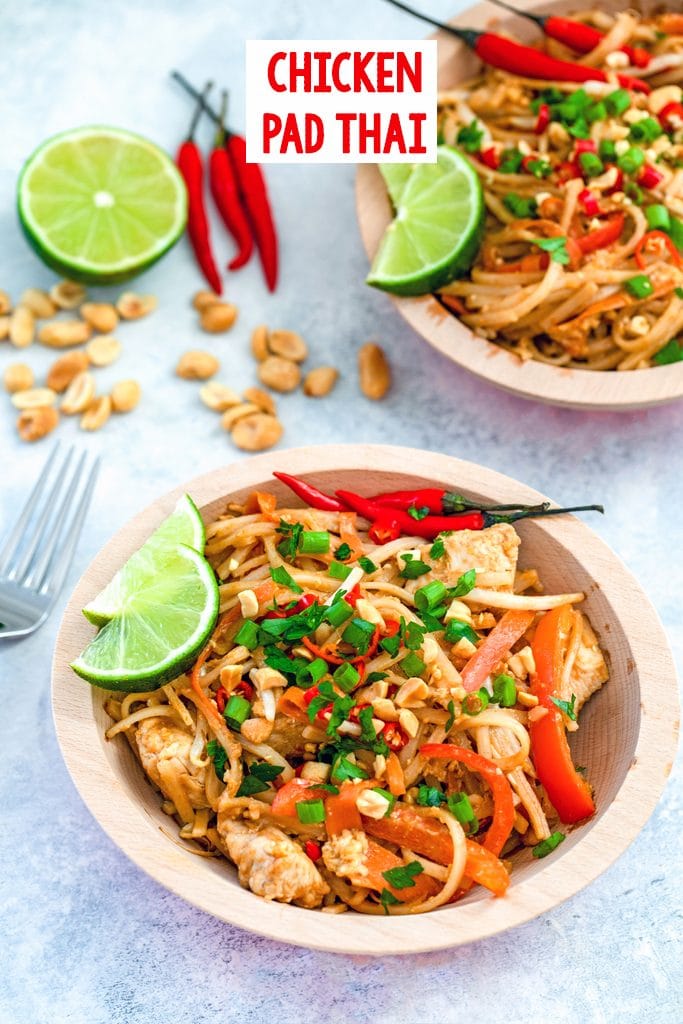 Overhead view of a bowl of Chicken pad Thai topped with scallions red chili peppers, peanuts, and limes, with peanuts, limes, peppers, and a second bowl of Pad Thai in the background and recipe title at top