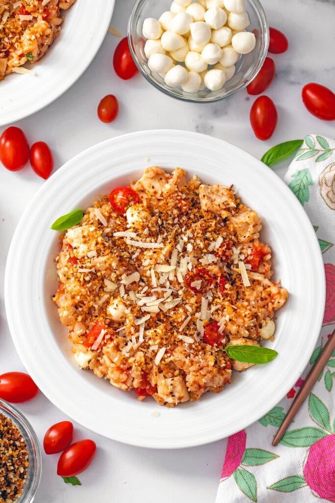 Overhead view of a bowl of chicken parmesan risotto topped with crispy panko with cherry tomatoes and mozzarella balls all round