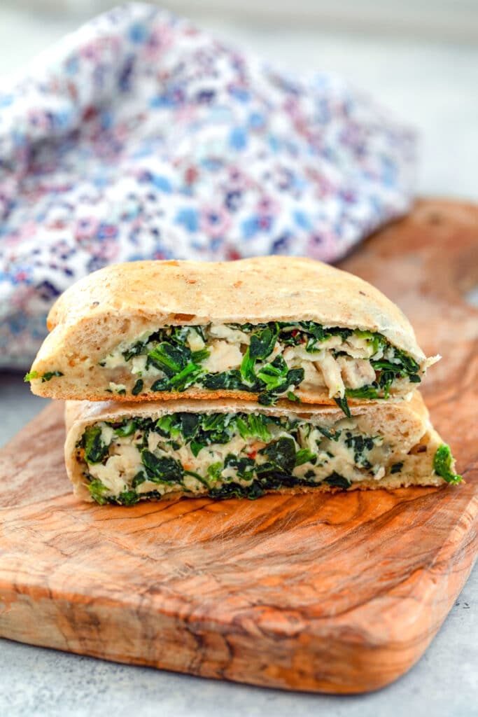Head-on view of a chicken and spinach calzone cut in half and stacked on a wood cutting board