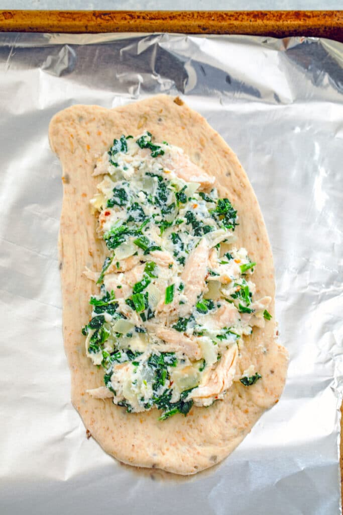 View of dough rolled into an oval with chicken spinach mixture in the center