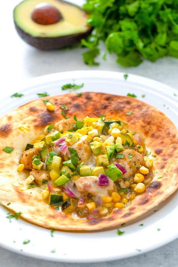 Overhead close-up of chicken and summer vegetable tostadas with avocado half and cilantro in background