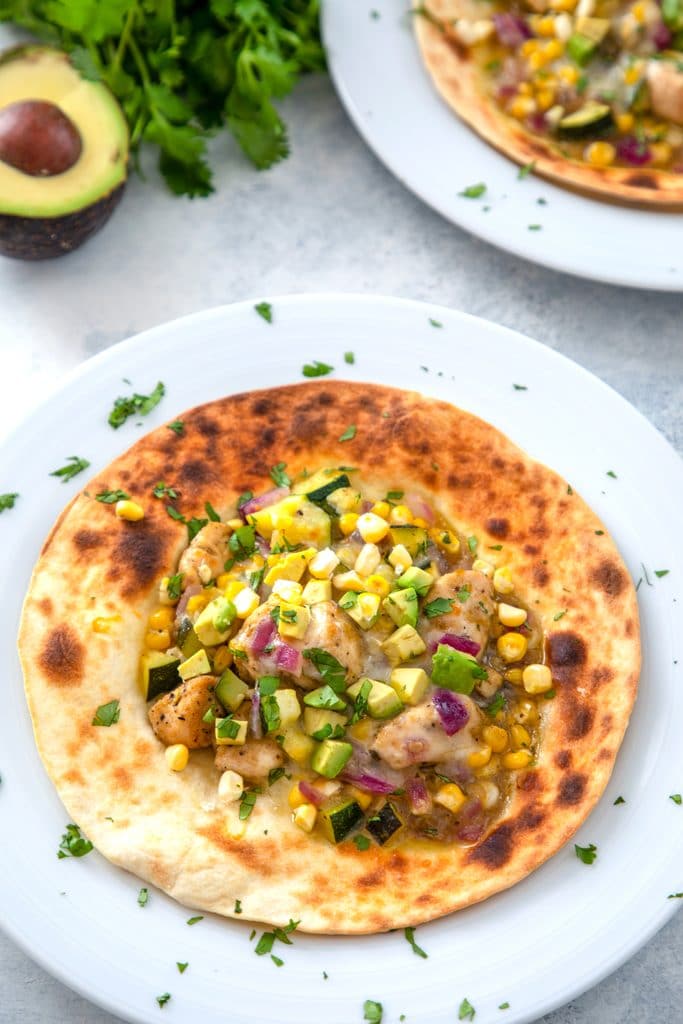 Overhead view of chicken and summer vegetable tostadas topped with avocado and cheese with avocado and cilantro in the background