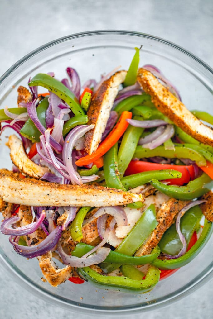 Overhead view of cooked chicken and veggies tossed together in a bowl