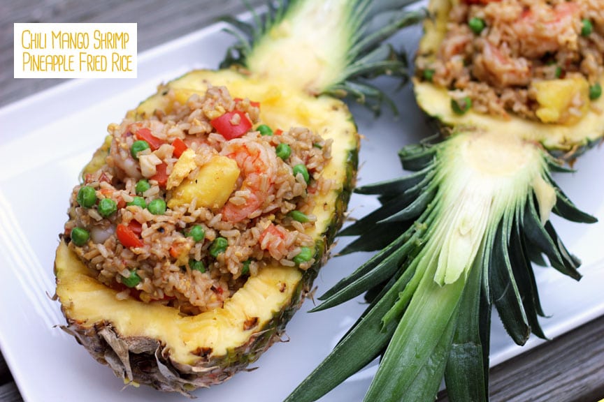 Two pineapple halves filled with chili mango shrimp pineapple fried rice served on a white platter with "Chili Mango Shrimp Pineapple Fried Rice" text at the top