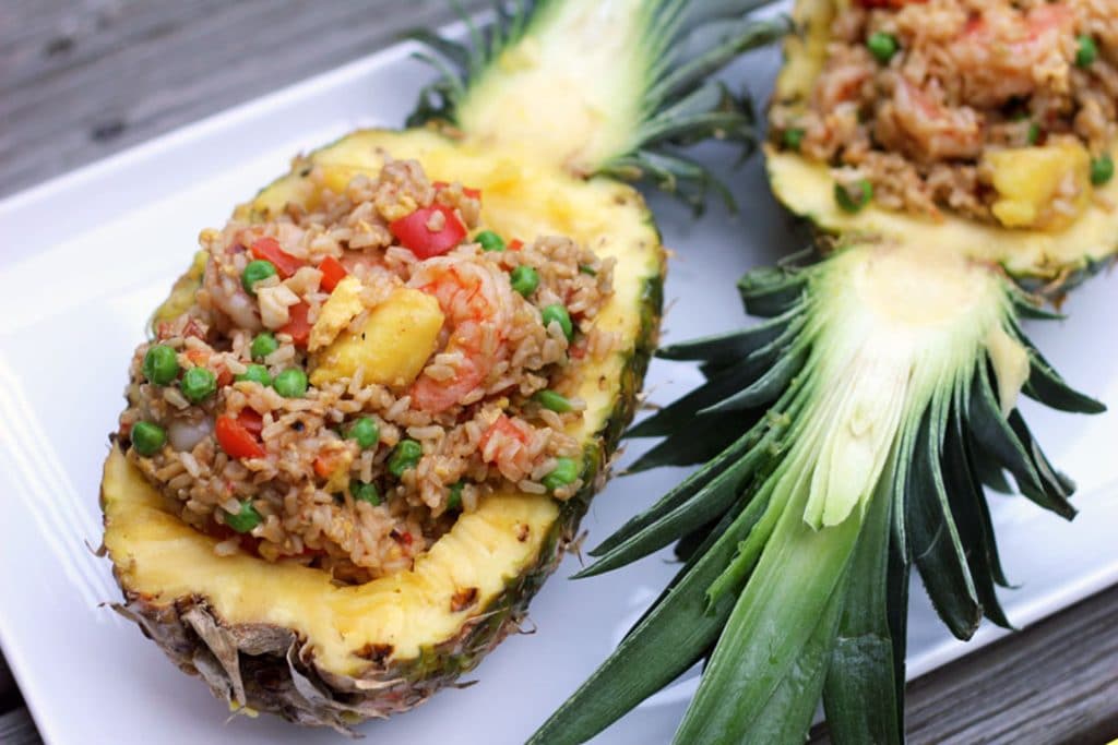 Two pineapple halves filled with chili mango shrimp pineapple fried rice served on a white platter