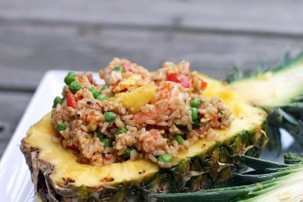 A close-up of chili mango shrimp pineapple fried rice served in half of a hollowed out pineapple on a white platter