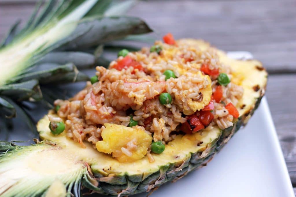 Close up of upside down pineapple half, hollowed out and filled with chili mango shrimp pineapple fried rice