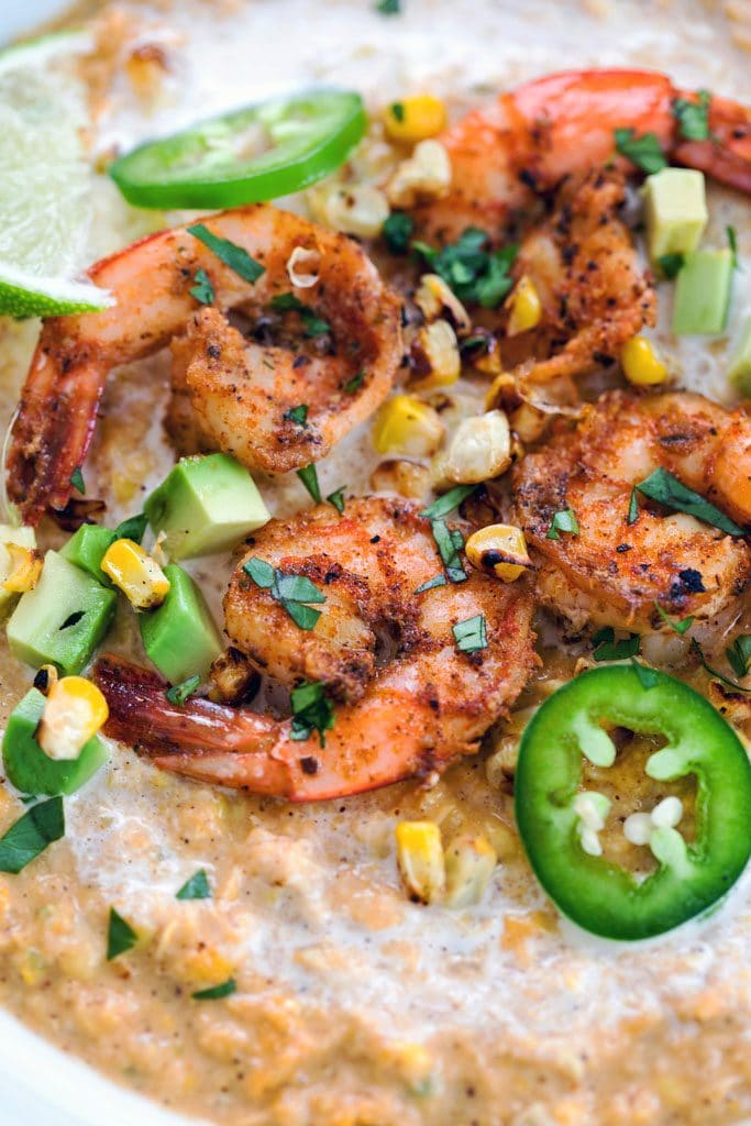 Close-up of the spicy shrimp sitting on top of the Mexican corn bisque, surrounded by jalapeño slices, grilled corn kernels, diced avocado, a lime wedge, and chopped cilantro