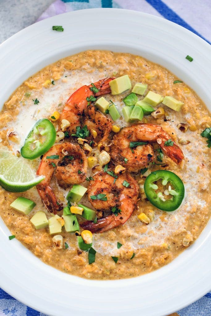 Bird's eye view closeup of Mexican corn bisque topped with spicy shrimp, sliced jalapeños, grilled corn kernels, lime wedges, and chopped cilantro in a white bowl