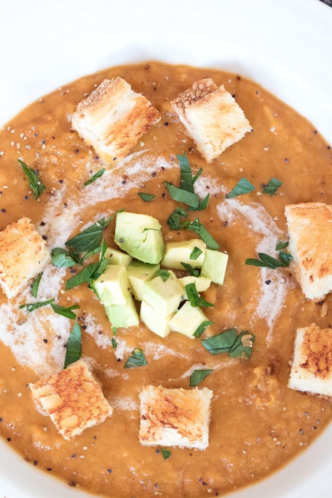 Overhead closeup view of chipotle butternut squash soup with grilled cheese croutons, chopped avocado, and chopped parsley on top