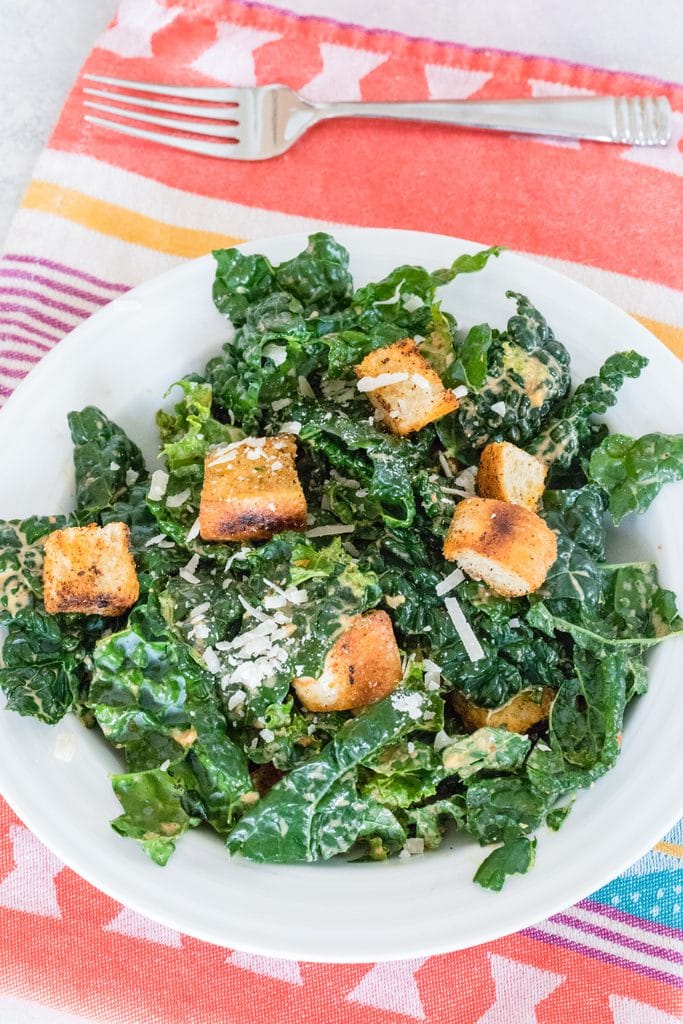 Closeup photo from above of chipotle kale Caesar salad on red towel with fork in back