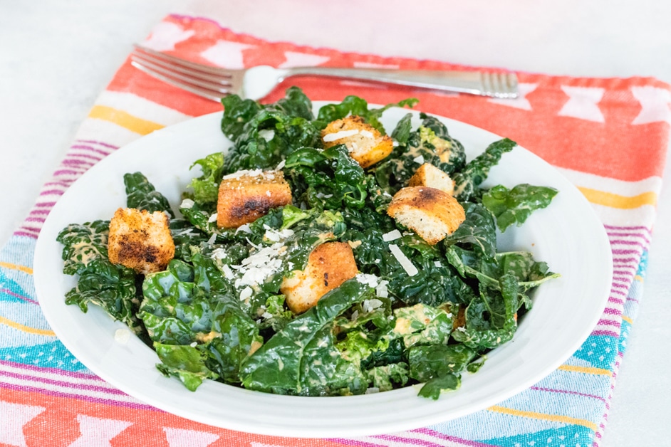 Horizontal photo of chipotle kale Caesar salad on red, yellow, and blue towel, with fork in the background