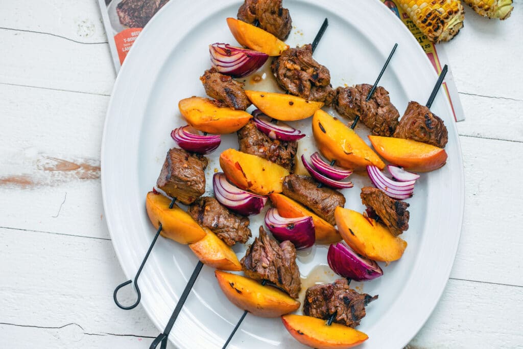 Landscape bird's eye view of chipotle steak and peach kabobs with red onion on white platter