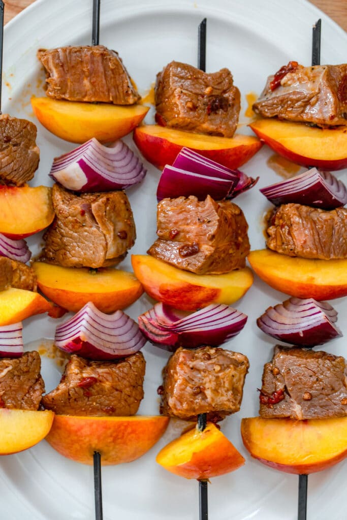 Overhead view of steak and peach kabobs on platter ready to be grilled