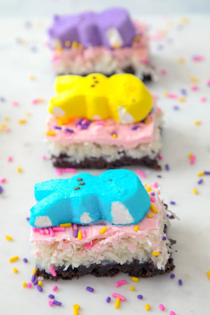 Head-on view of a row of Peeps brownie bars with coconut, pink icing, and Peeps on top with sprinkles all around