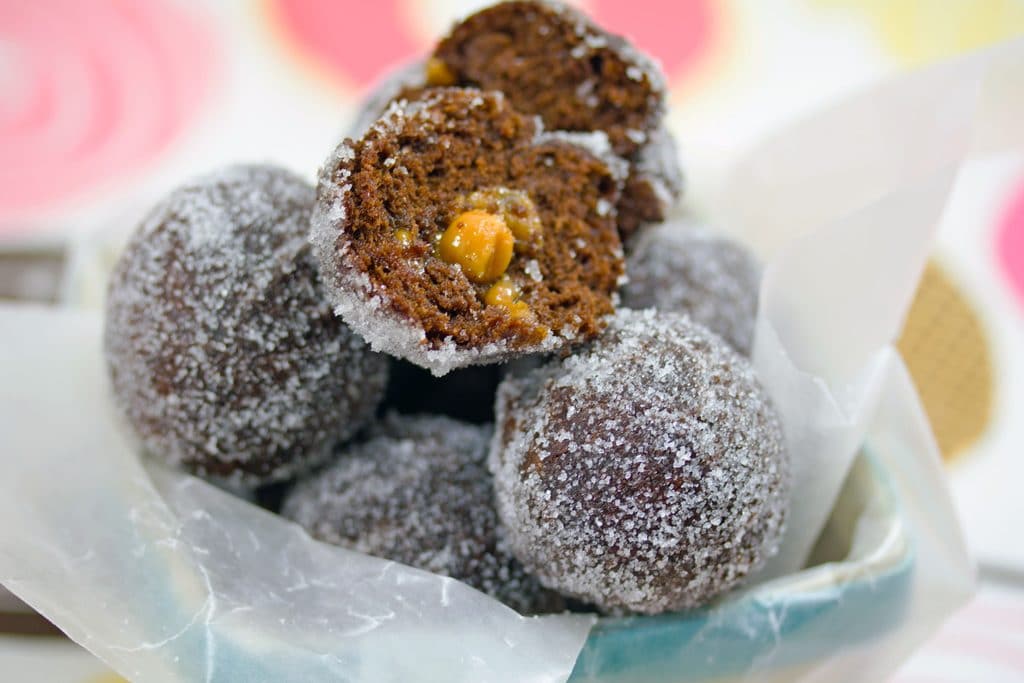 Close-up of basket of chocolate caramel doughnut holes with top doughnut cut open to show caramel oozing out