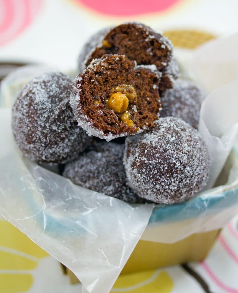 Arial view of basket full of chocolate caramel doughnut holes with top doughnut cut open to show caramel oozing out