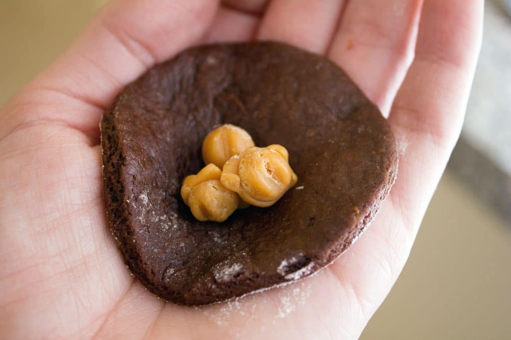 Chocolate dough round being held in palm of hand with caramel bits in the middle of it