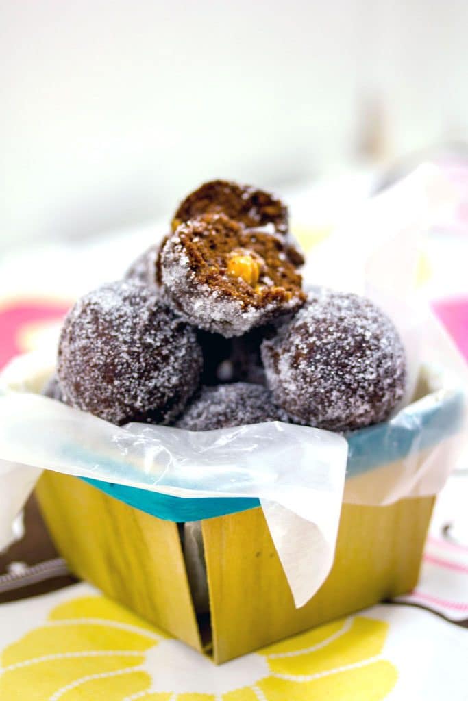 Chocolate caramel doughnut holes stacked in a basket with the top one cut open with caramel oozing out 