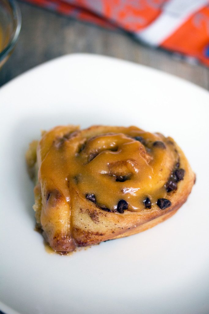 Overhead view of a chocolate chip cinnamon roll with butterscotch icing on a small white plate