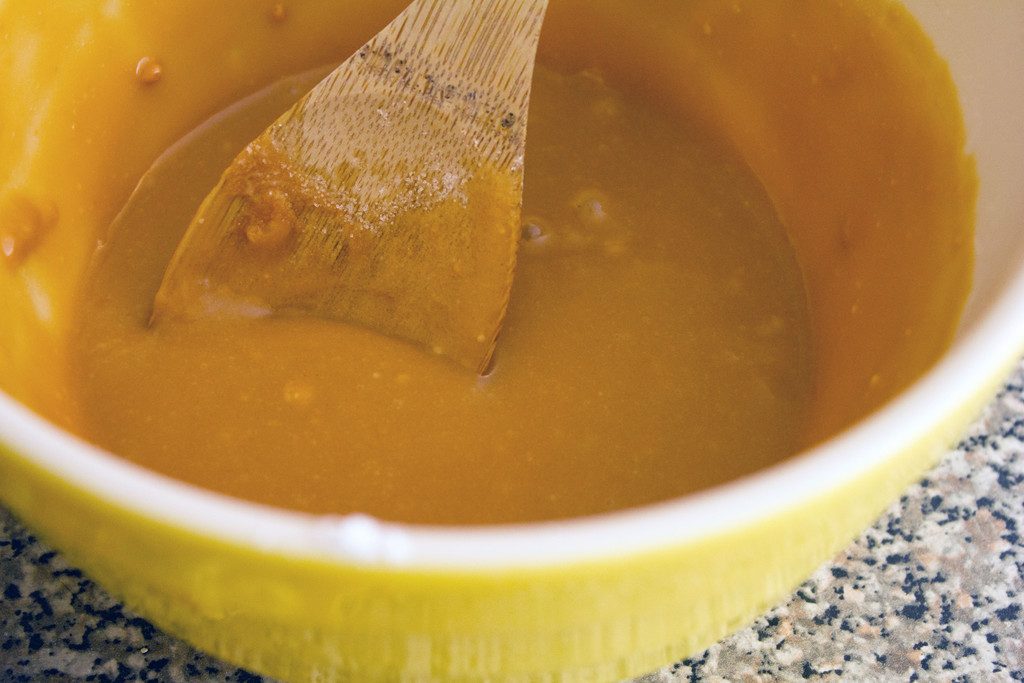 Overhead view of smooth butterscotch icing in mixing bowl with wooden spoon
