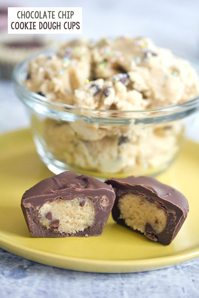 Head-on view of a chocolate-covered chocolate chip cookie dough cup cut in half on a yellow plate with bowl of cookie dough with sprinkles in the background and recipe title at top