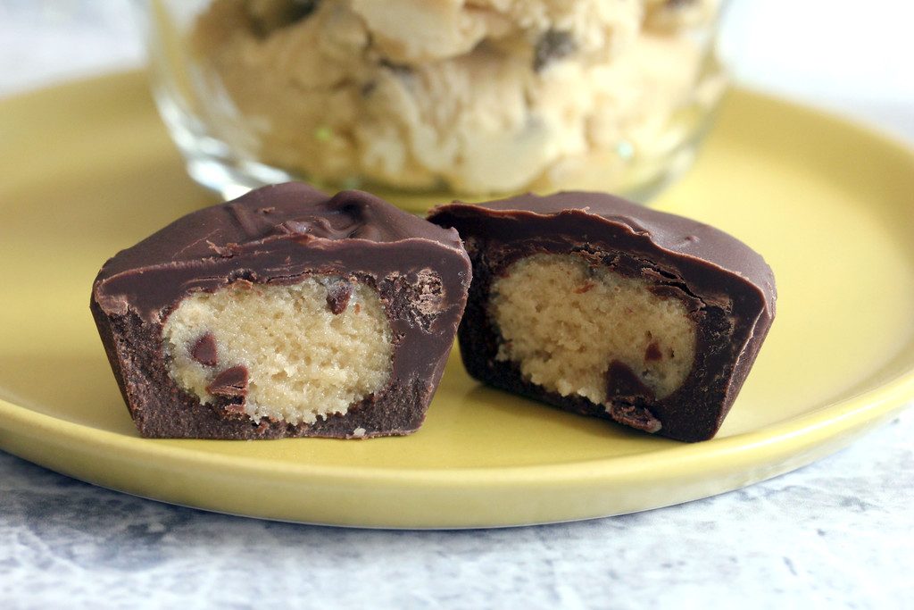 Landscape closeup view of a chocolate-covered chocolate chip cookie dough cup on a yellow plate