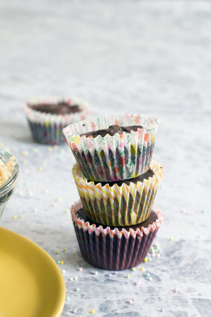 Head-on view of three chocolate chip cookie dough cups in spring baking papers stacked on top of each other on marble surface