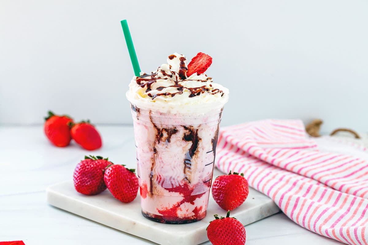 Landscape head-on view of chocolate covered strawberry frappuccino in a Starbucks cup with straw and strawberries all around.