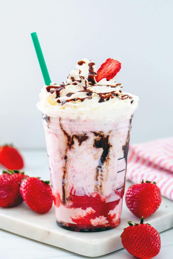 Head-on view of a chocolate covered strawberry frappuccino with strawberry and mocha syrup and a whipped cream topping with strawberries all around.