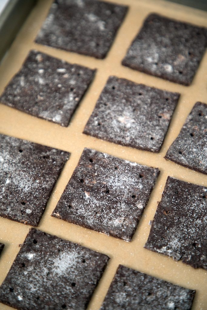 Overhead view of chocolate graham cracker dough sliced into squares on baking sheet ready for oven