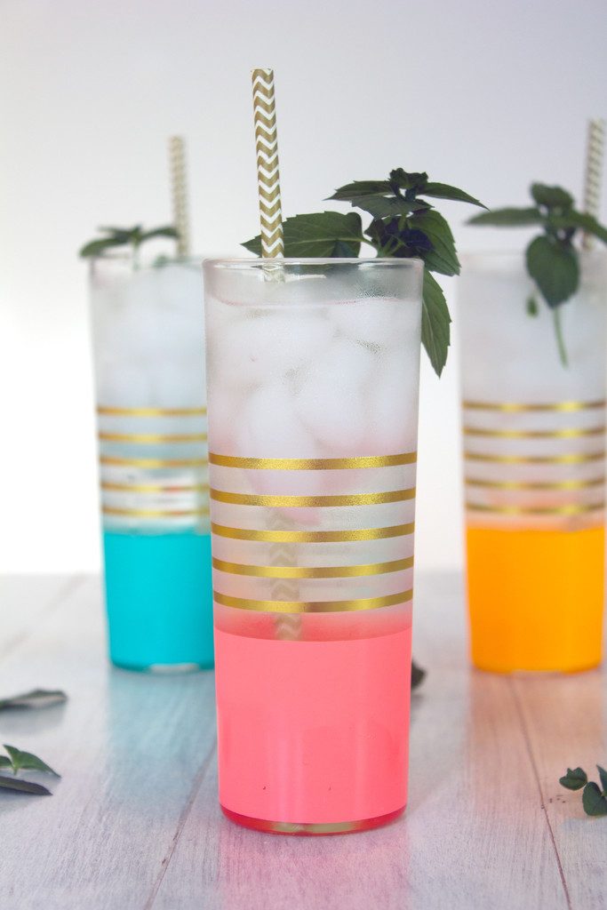 Head-on view of a pink and gold glass filled with chocolate mint coconut gin soda with gold and white straw and fresh chocolate mint with more cocktails in the background