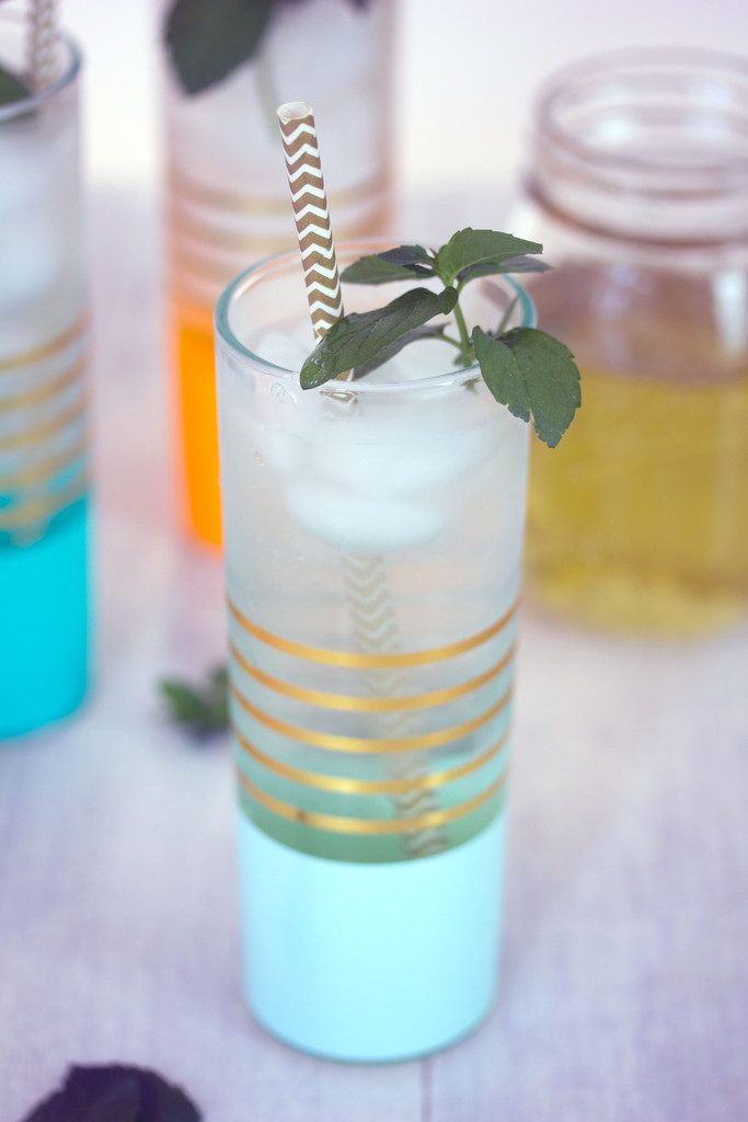 Overhead view of teal and gold glass with chocolate mint coconut gin soda with gold and white straw and fresh mint with more cocktails and jar of simple syrup in background