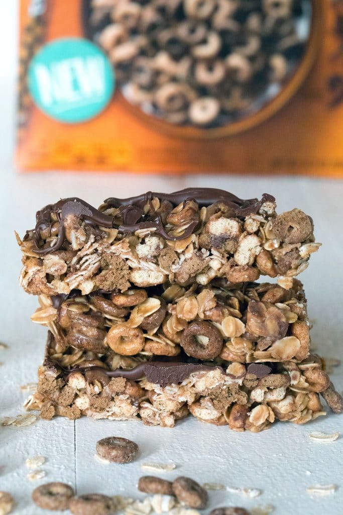 Head-on view of a stack of three chocolate peanut butter cheerios granola bars with box of Cheerios in the background