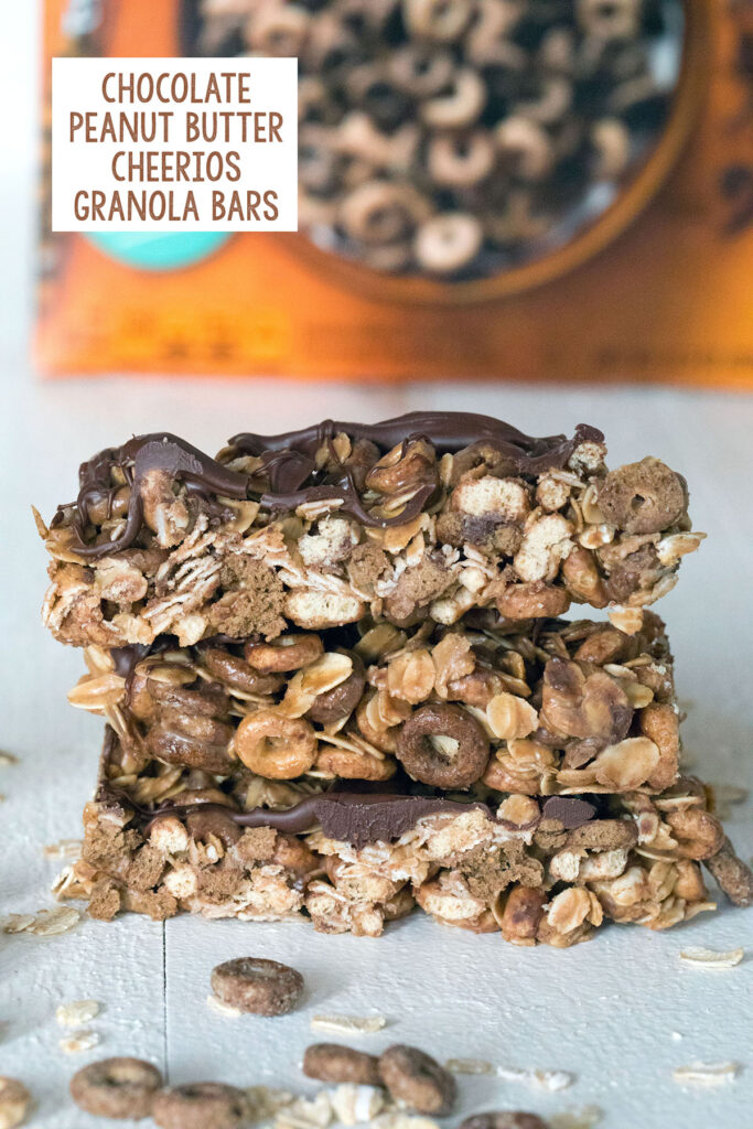 Head-on view of a stack of three chocolate peanut butter cheerios granola bars with box of Cheerios in the background and recipe title at top