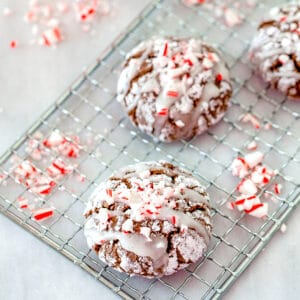 Overhead view of chocolate peppermint sour cream crinkle cookies on a cooling rack with crushed candy canes and a container of sour cream in the background